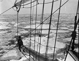 The Discovery passing through loose pack off MacRobertson Land, with a man sitting on the bowsprit